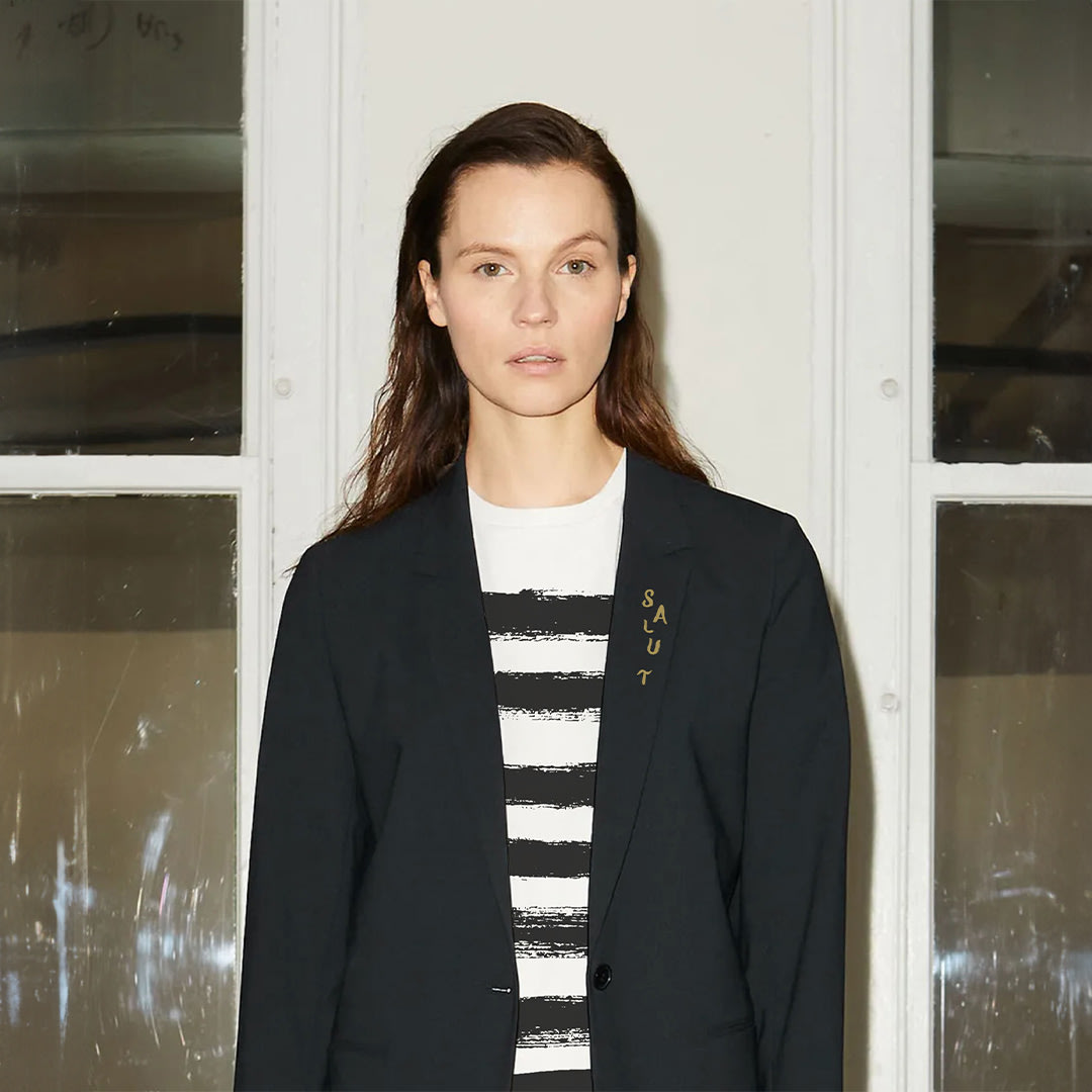 A model wearing a shirt with horizontal Frenchy hand painted stripes, and a blazer with the Frenchy typeface that says "salut" on the breast collar.