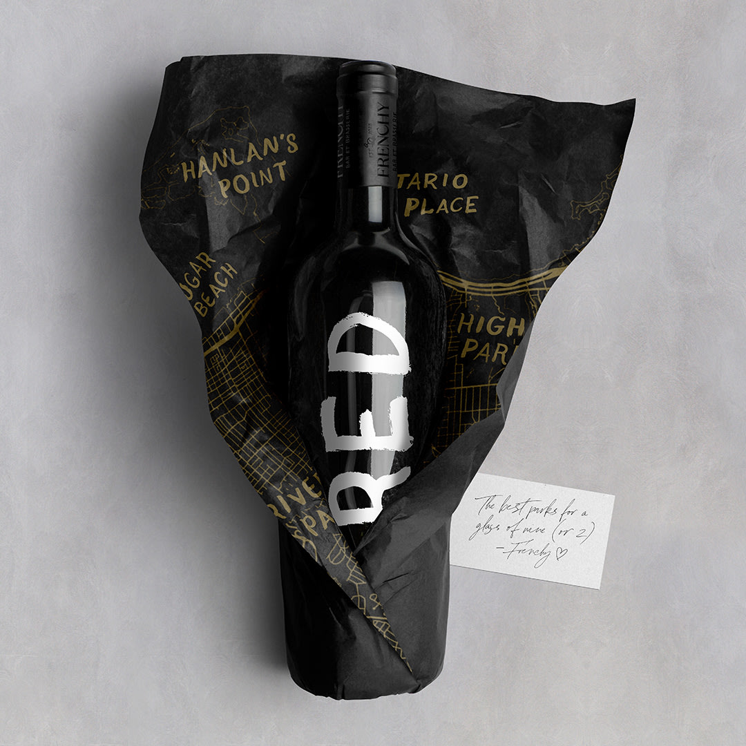 A wine bottle that reads "red" in the Frenchy hand painted font, wrapped in a Frenchy branded map of Toronto.